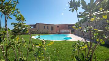 A swimming pool surrounded by a well-maintained lawn and a stone wall.