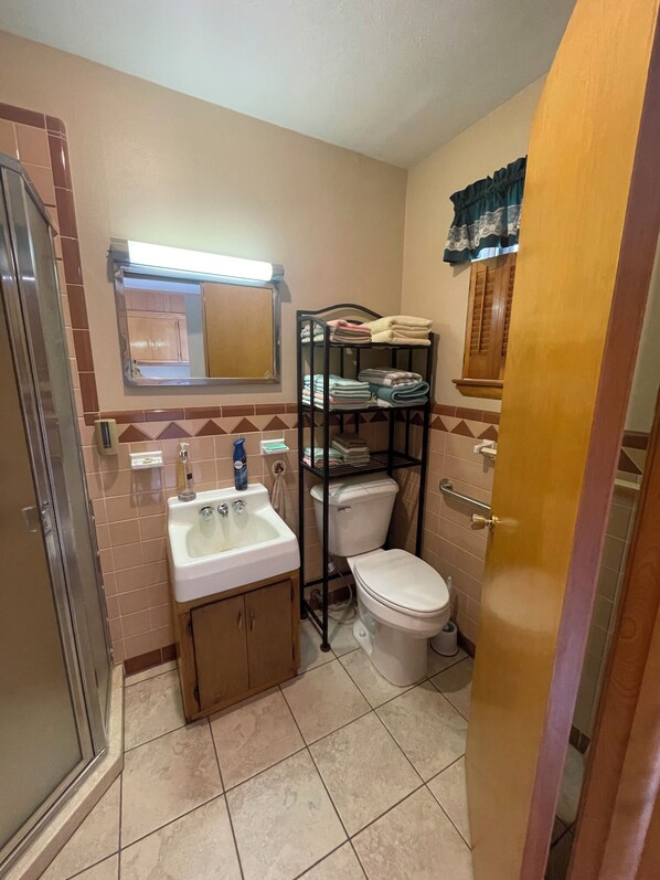 A compact bathroom with a sink, toilet, and a shelf with folded towels.
