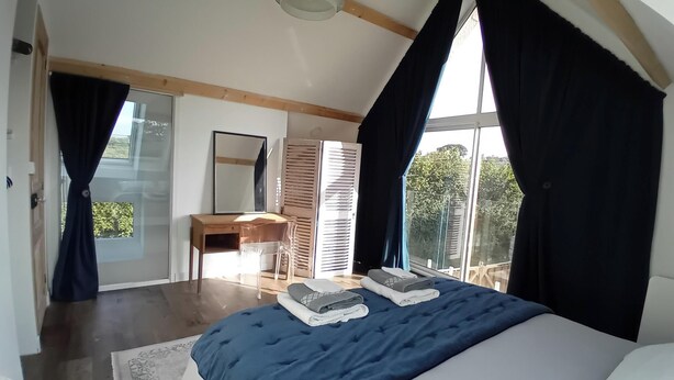 Un dormitorio con una cama grande, un escritorio, una silla y un ventanal con cortinas.