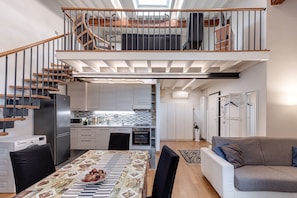 A modern apartment with a kitchen, dining area, and a staircase leading to a loft bedroom.
