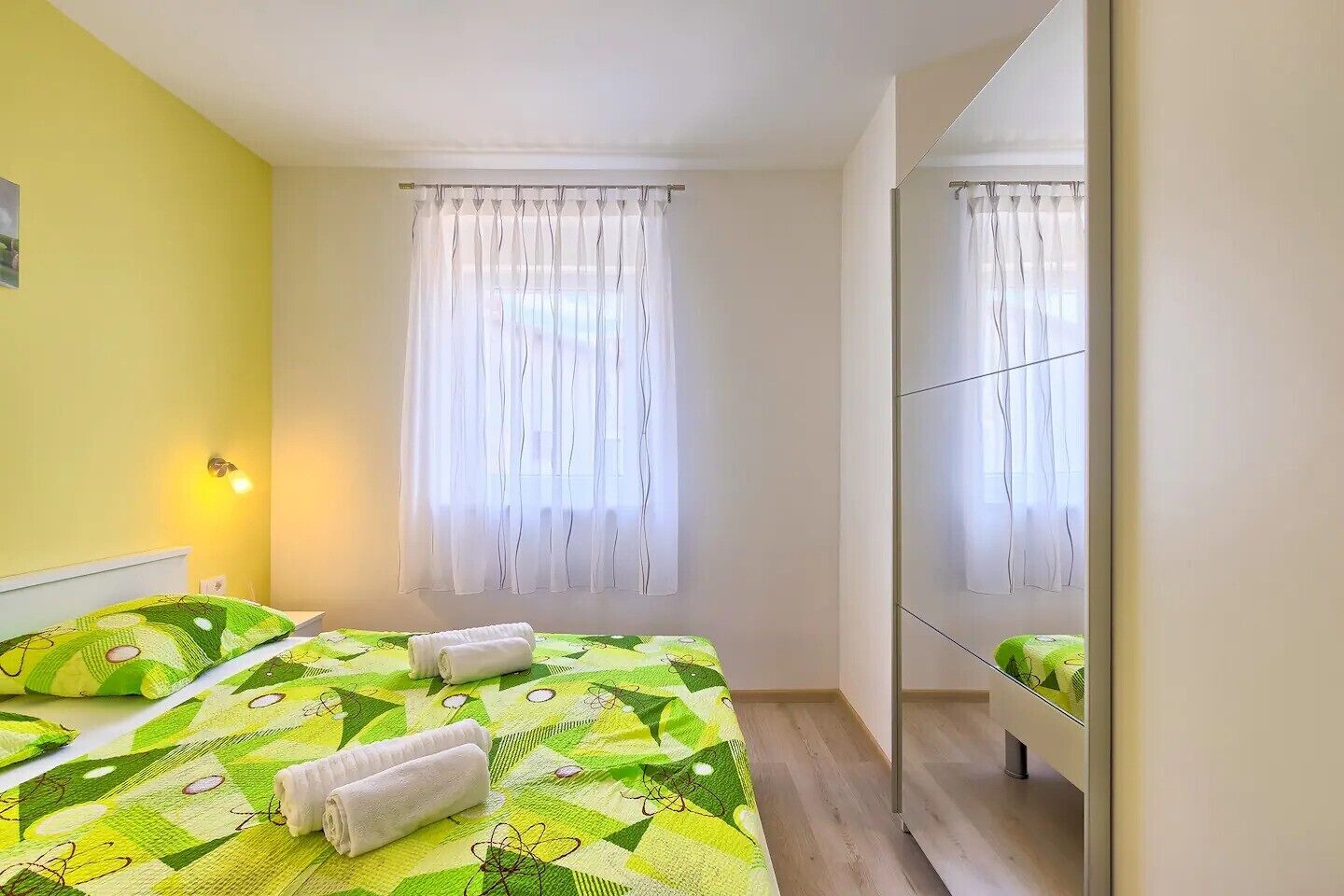 Una habitación de hotel con cama, espejo y ventana con cortinas.