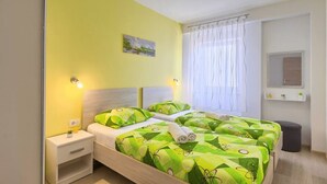 A double bed with green and white bedding, a bedside table with a lamp, a small plant, and a window with white curtains. - Apartment Viola in center of Medulin for 6 person (Medulin)