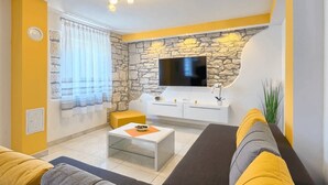 A living room with a stone accent wall, a flat-screen TV, a white console table, and a yellow sofa. - Apartment Viola in center of Medulin for 6 person (Medulin)