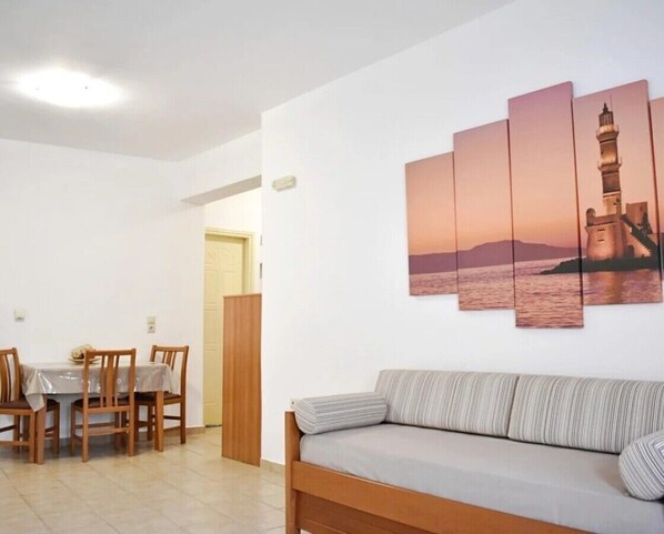A room with a dining table, chairs, a sofa, and a wall-mounted artwork of a lighthouse.
