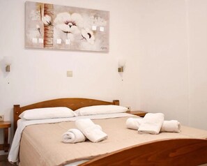 A neatly made bed with white linens and rolled towels, a wooden headboard, and a painting above the bed.