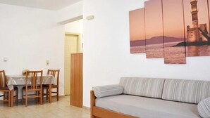 Ein Wohnzimmer mit einer Couch, einem Esstisch mit Stühlen und einem an der Wand hängenden Bild eines Leuchtturms.