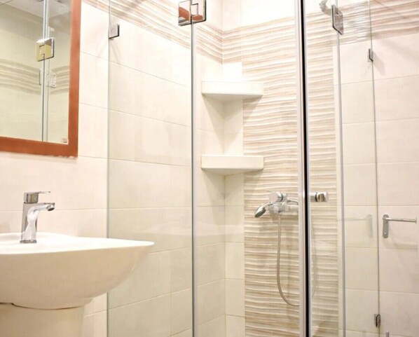A bathroom with a sink, mirror, and glass-enclosed shower area.