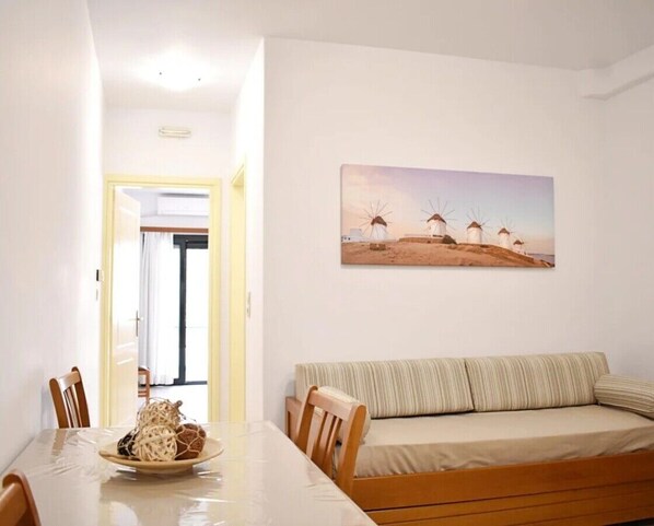 A dining area with a table, chairs, and a plate of food. There is a sofa and a painting of windmills on the wall.