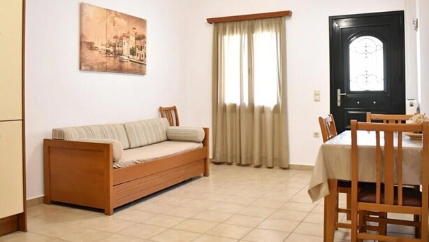 Una sala de estar con sofá, mesa de comedor, sillas, un cuadro y una puerta.