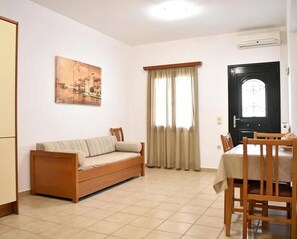 A living room with a sofa, dining table, chairs, a painting, and a door.