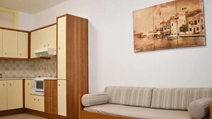 Un espacio habitable compacto con kitchenette, un sofá y un cuadro colgado en la pared.