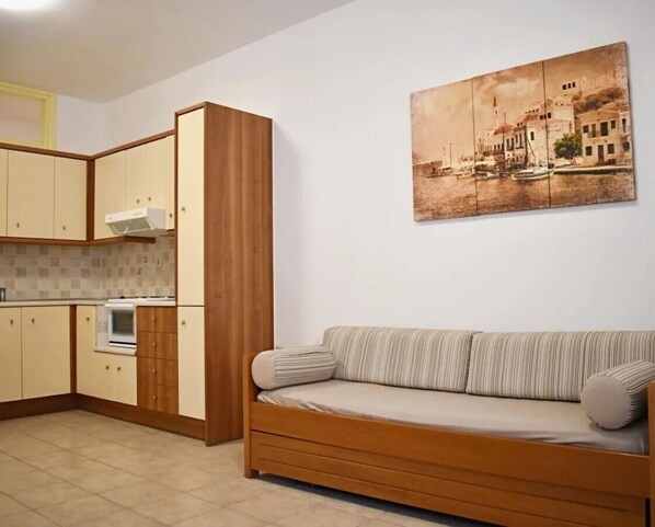 A compact living space with a kitchenette, a sofa, and a wall-mounted painting.
