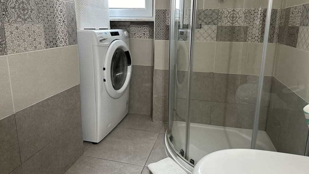 Ein kleines Badezimmer mit Waschmaschine, Duschkabine aus Glas und Toilette.