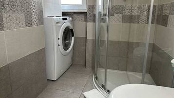 Ein kleines Badezimmer mit Waschmaschine, Duschkabine aus Glas und Toilette.