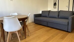 A living room with a grey sofa, white chairs, and a wooden dining table. - Suite&Chic Apartment (Bari)
