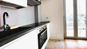 A modern kitchen with a black countertop, white cabinets, a stainless steel range hood, and a large window with a view of buildings. - Suite&Chic Apartment (Bari)