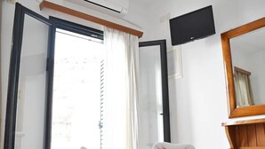 A hotel room with a bed, a flat-screen TV, a large mirror, and a window with curtains. - Apartment 'Manolika Studio 4' with Sea View, Wi-Fi and Air Conditioning (Kythnos)