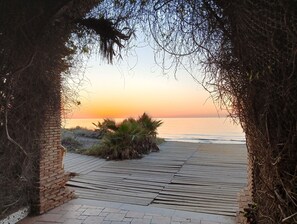 Un sentier en bois mène à une plage d’où l’on peut admirer le coucher de soleil sur l’océan.