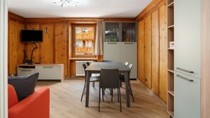 A compact kitchen with a dining table, chairs, a TV, and wooden cabinetry. - Apartment "Casa Picchio" with Mountain View and Balcony (Rabbi)