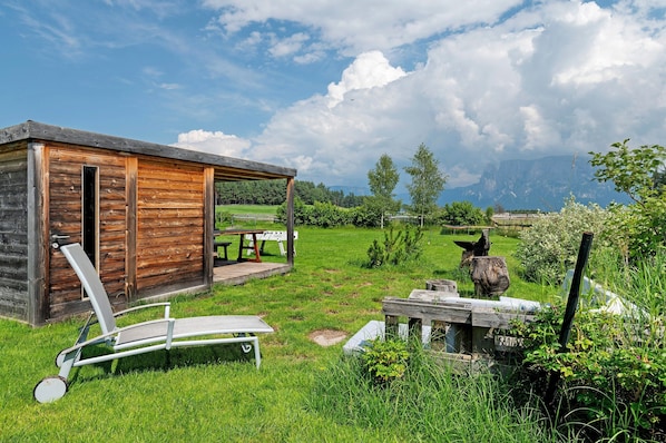 A rustic wooden cabin with a covered porch, a lounge chair, and a picnic table.