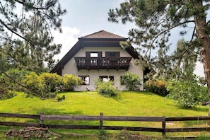 A two-story house with a balcony, surrounded by a wooden fence and greenery.
