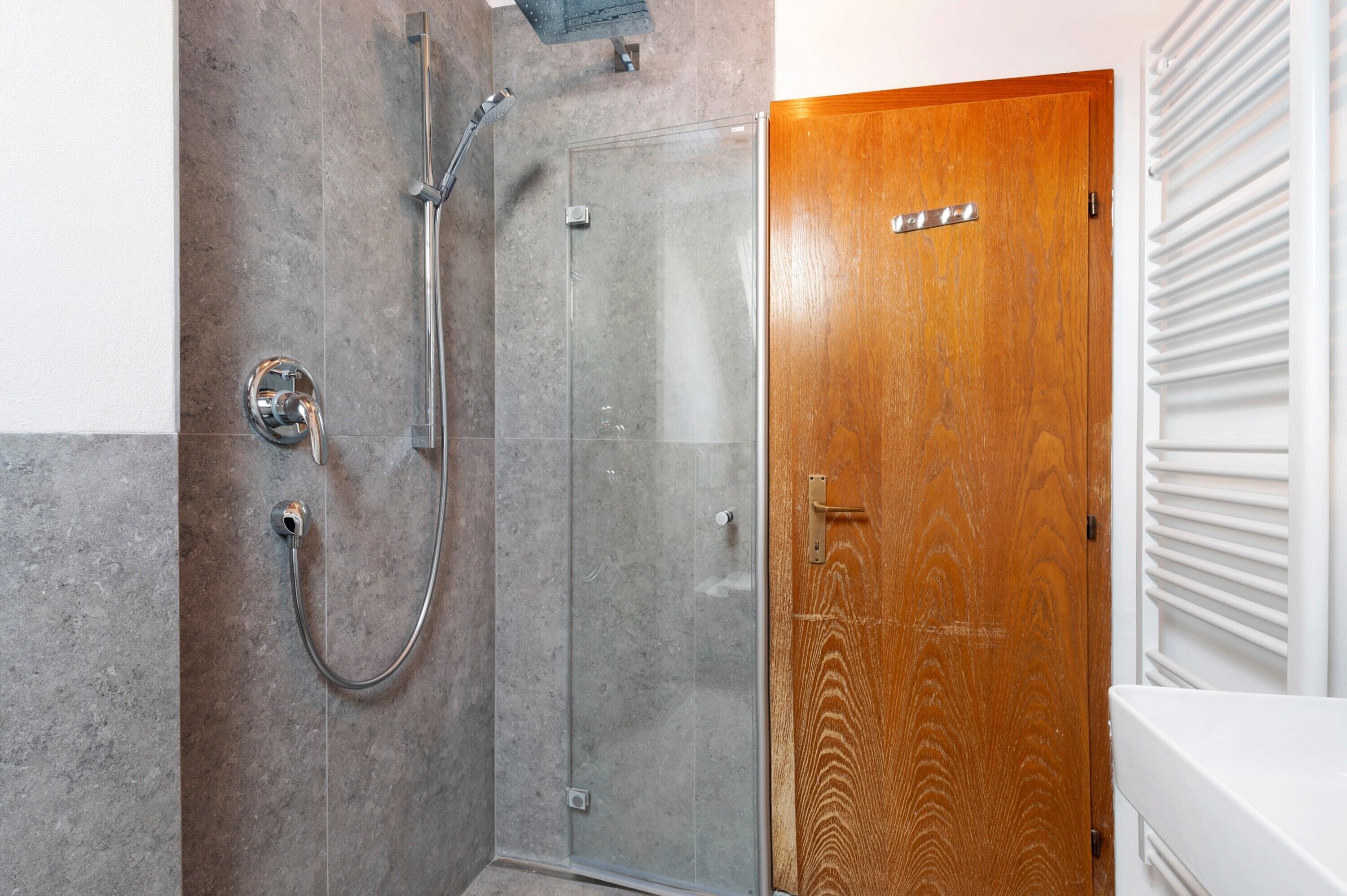 Baño con ducha, puerta de madera y radiador blanco.