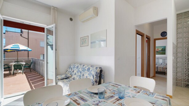 A dining area with a table set for two, a sofa, and a balcony with outdoor seating. - Apartment 'Residence International' with Private Terrace, Balcony and Air Conditioning (Lido di Jesolo)