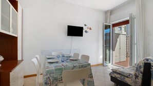 A dining area with a table set for four, a television mounted on the wall, and a sliding glass door leading to an outdoor area. - Apartment 'Residence International' with Private Terrace, Balcony and Air Conditioning (Lido di Jesolo)