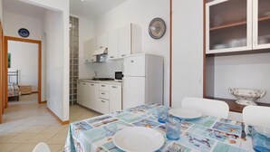 A dining area with a table set for two, a kitchen with white cabinets, and a decorative plate on the wall. - Apartment 'Residence International' with Private Terrace, Balcony and Air Conditioning (Lido di Jesolo)