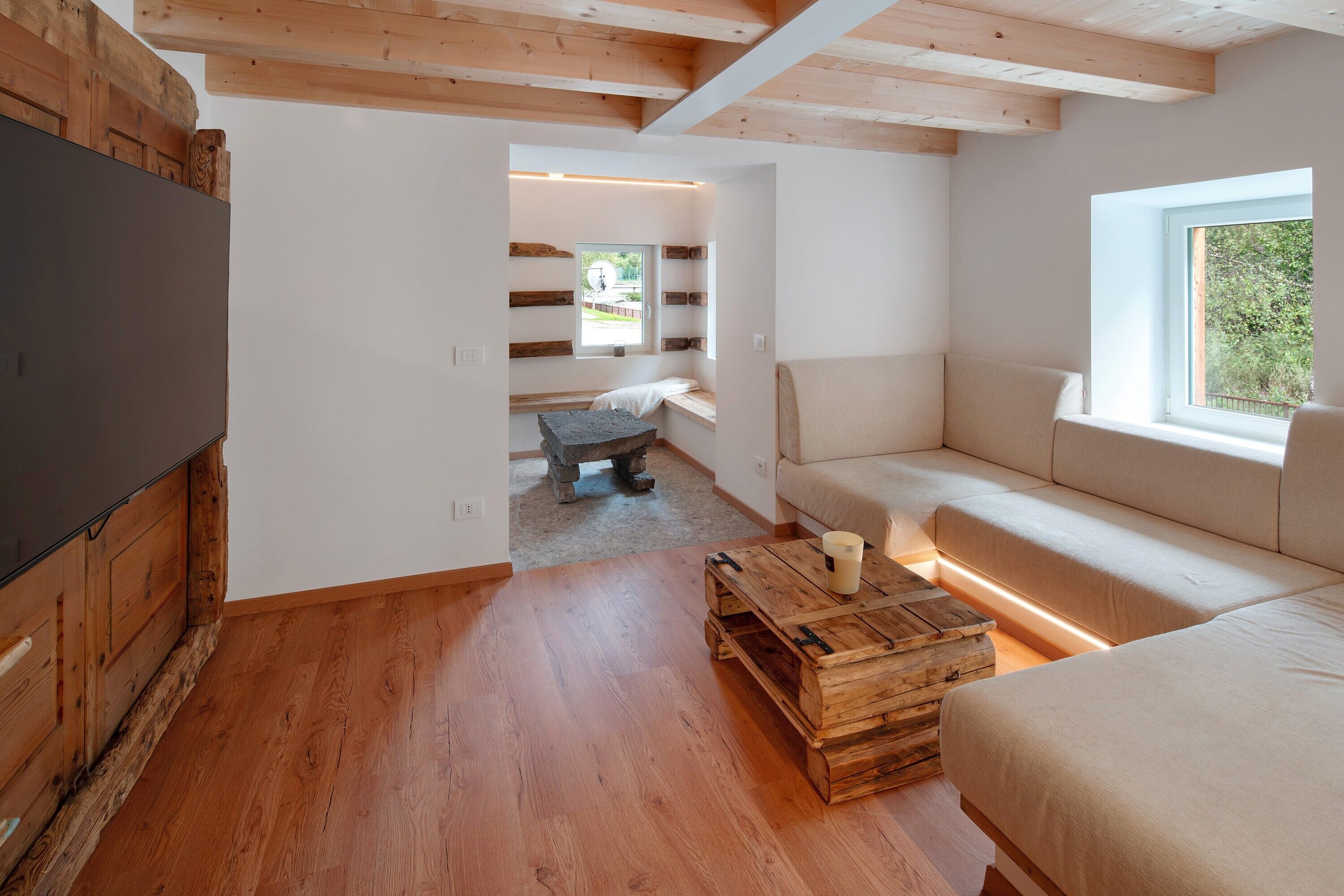 Habitació moderna amb terra de fusta, un sofà, una televisió i una finestra.