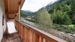 Un balcón de madera con vistas a un río y montañas.
