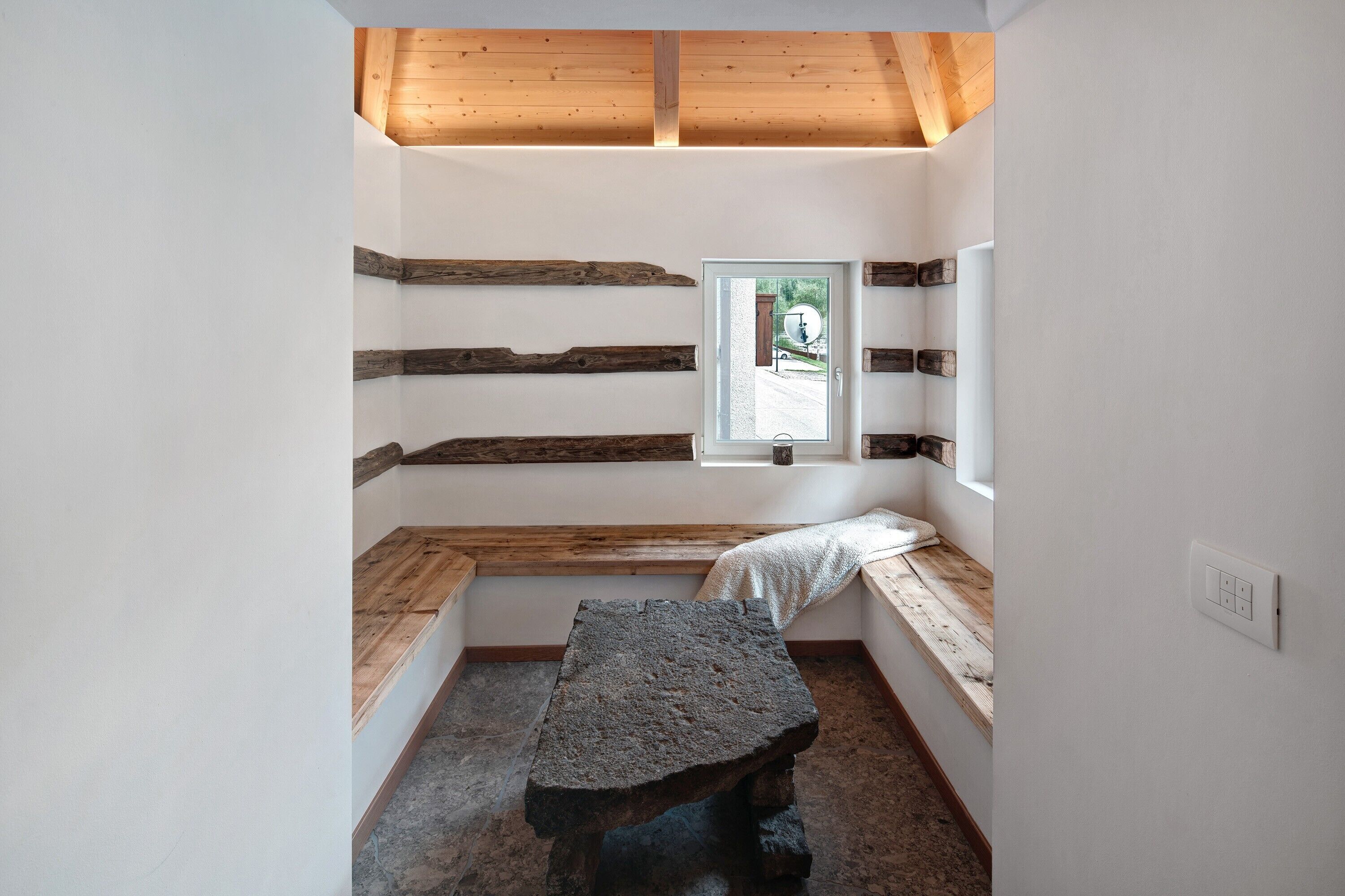 Une petite pièce étroite, avec un banc en pierre, des poutres en bois aux murs et une fenêtre donnant sur un paysage agréable.