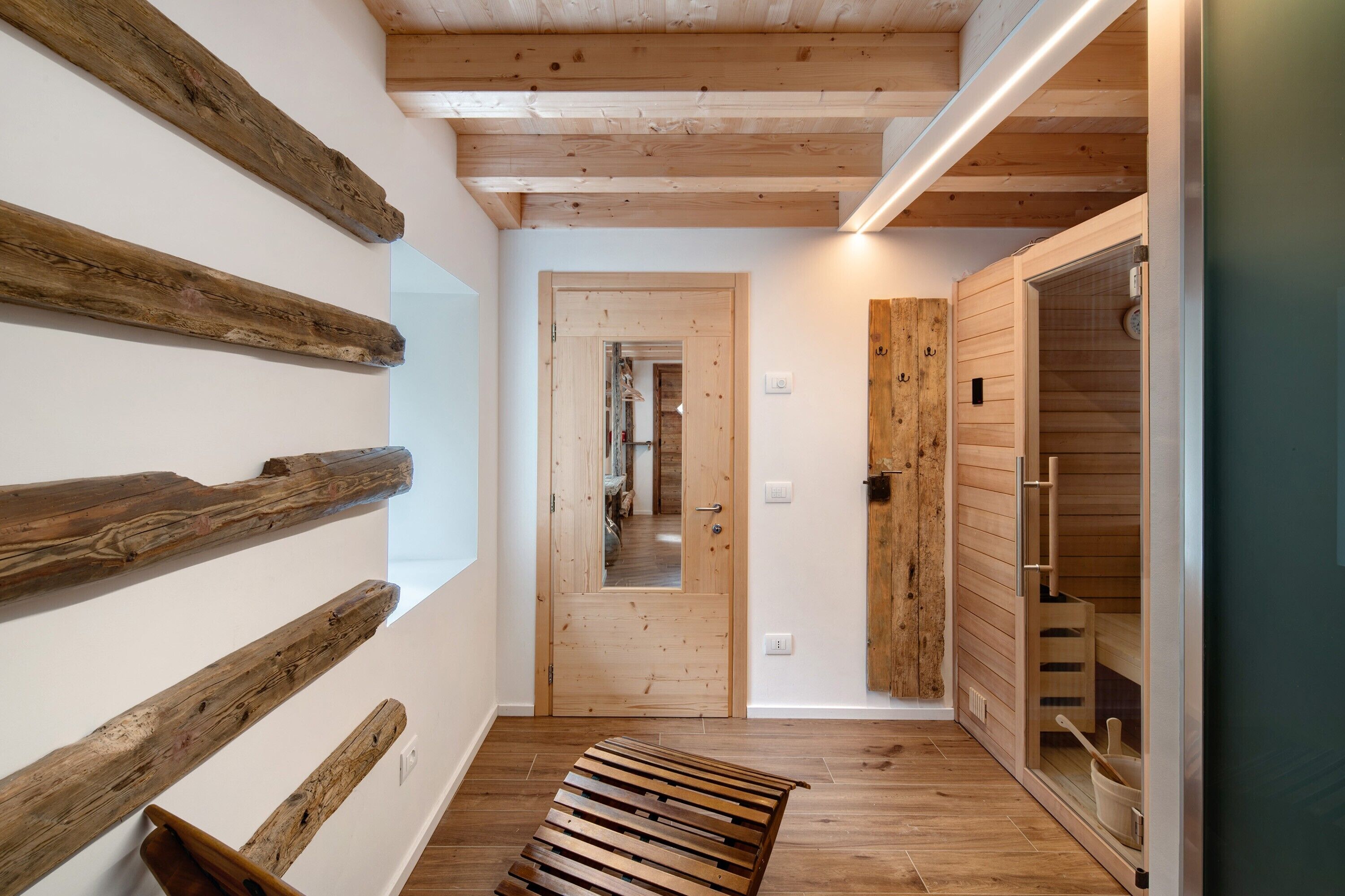 A wooden interior hallway with a bench, a wooden door, and a sauna room.