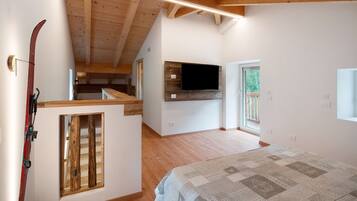 A bedroom with a bed, a mounted TV, wooden beams, a window, and a ski rack.