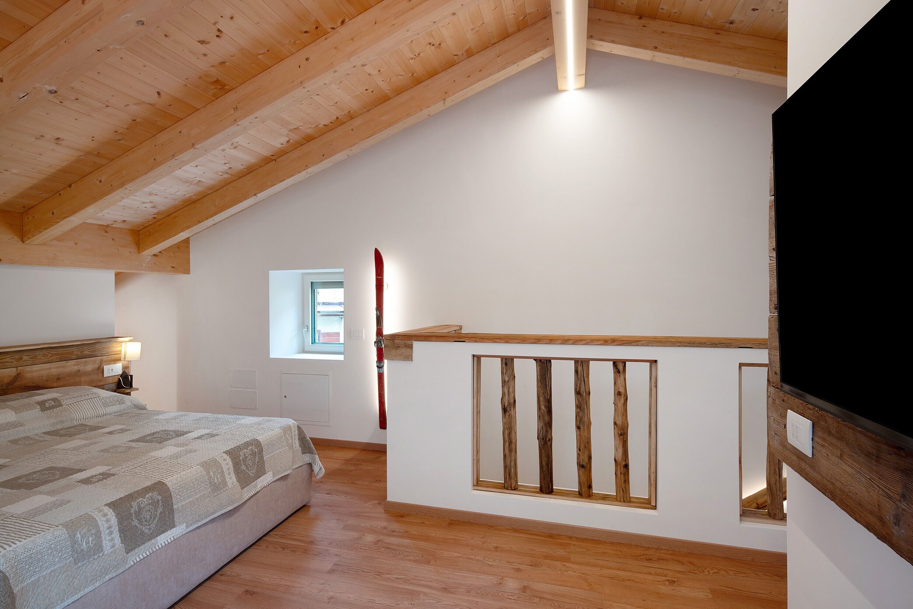A bedroom with a wooden ceiling, a bed, a window, and a TV.