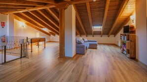 Habitación en ático con vigas de madera, un sofá, una mesa y una estantería.