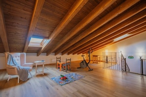 A spacious attic room with wooden beams, a skylight, a chair, a small table, a toy, and exercise equipment.