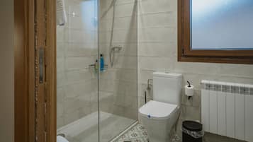 A bathroom with a glass-enclosed shower, a toilet, a radiator, and a trash bin.