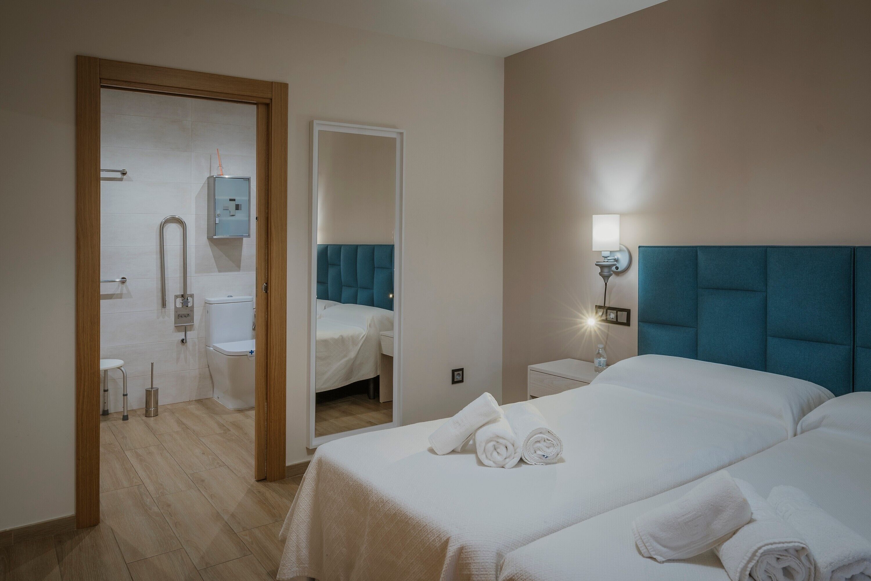 Habitación de hotel con cama, mesita de noche, espejo y baño visible a través de una puerta abierta.