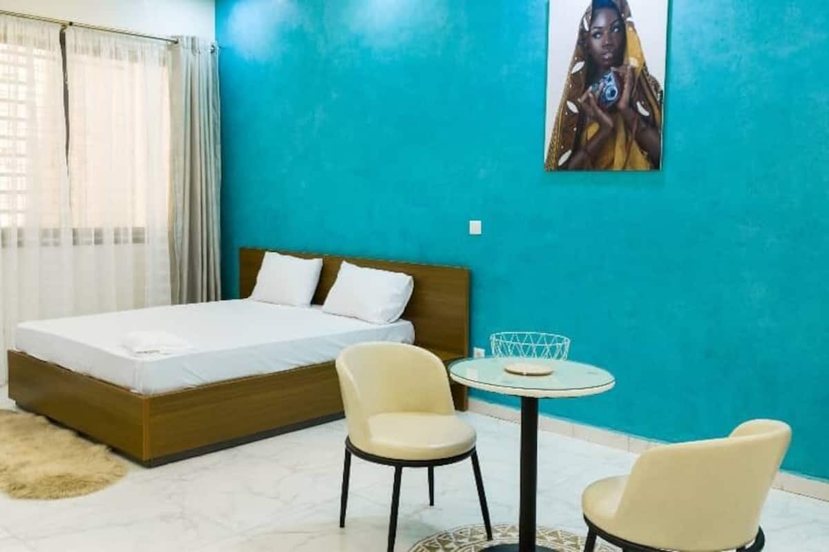 A bedroom with a bed, two chairs, a small table, and a painting on the wall.
