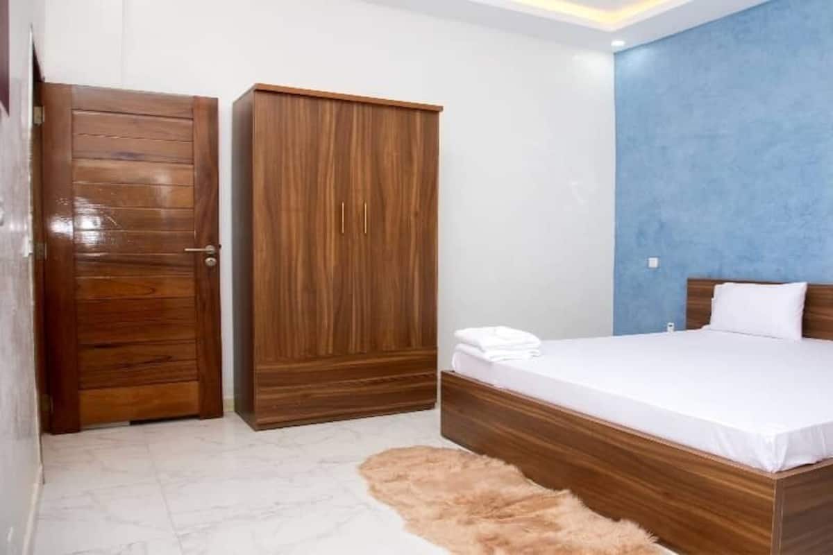 A bedroom with a wooden bed frame, a white mattress, and a blue accent wall.