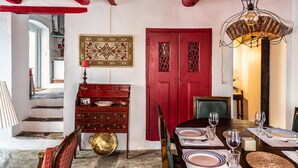 Een eetgedeelte met een tafel voor vier personen, een rode deur en een trap die naar een andere kamer leidt.