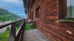 Una cabaña de madera con balcón, una mesa y sillas, con vista a una zona boscosa.