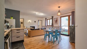 Una cocina moderna con zona de comedor, suelo de madera y un amplio ventanal con cortinas.