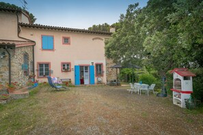 A house with a stone facade, a red-tiled roof, and a small patio area with outdoor furniture.