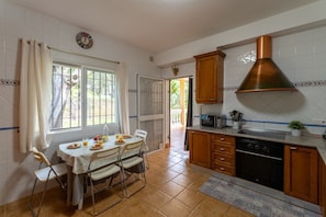 A kitchen with a dining table, chairs, a stove, and a large copper range hood.