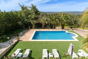 A rectangular swimming pool with a tiled edge, surrounded by a well-maintained lawn and several white lounge chairs.