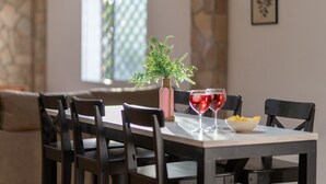 Una mesa de comedor con sillas, un florero con follaje, dos copas de vino y un tazón de papas fritas.
