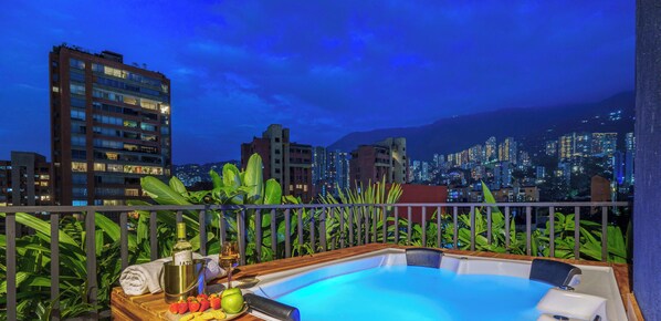 Piscina en la azotea con vista a la ciudad, rodeada de exuberante vegetación.