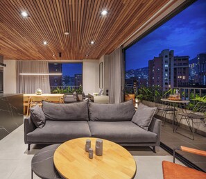 Ein modernes Wohnzimmer mit einem grauen Sofa, einem Holztisch und Blick auf die Stadt durch große Fenster.